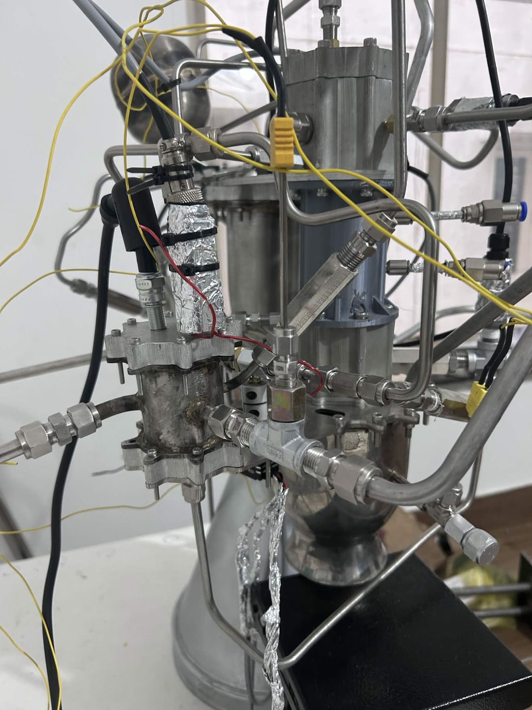 Close-up of APEX propulsion development hardware with flanged metal sections, fluid fittings, yellow connectors and cabling.