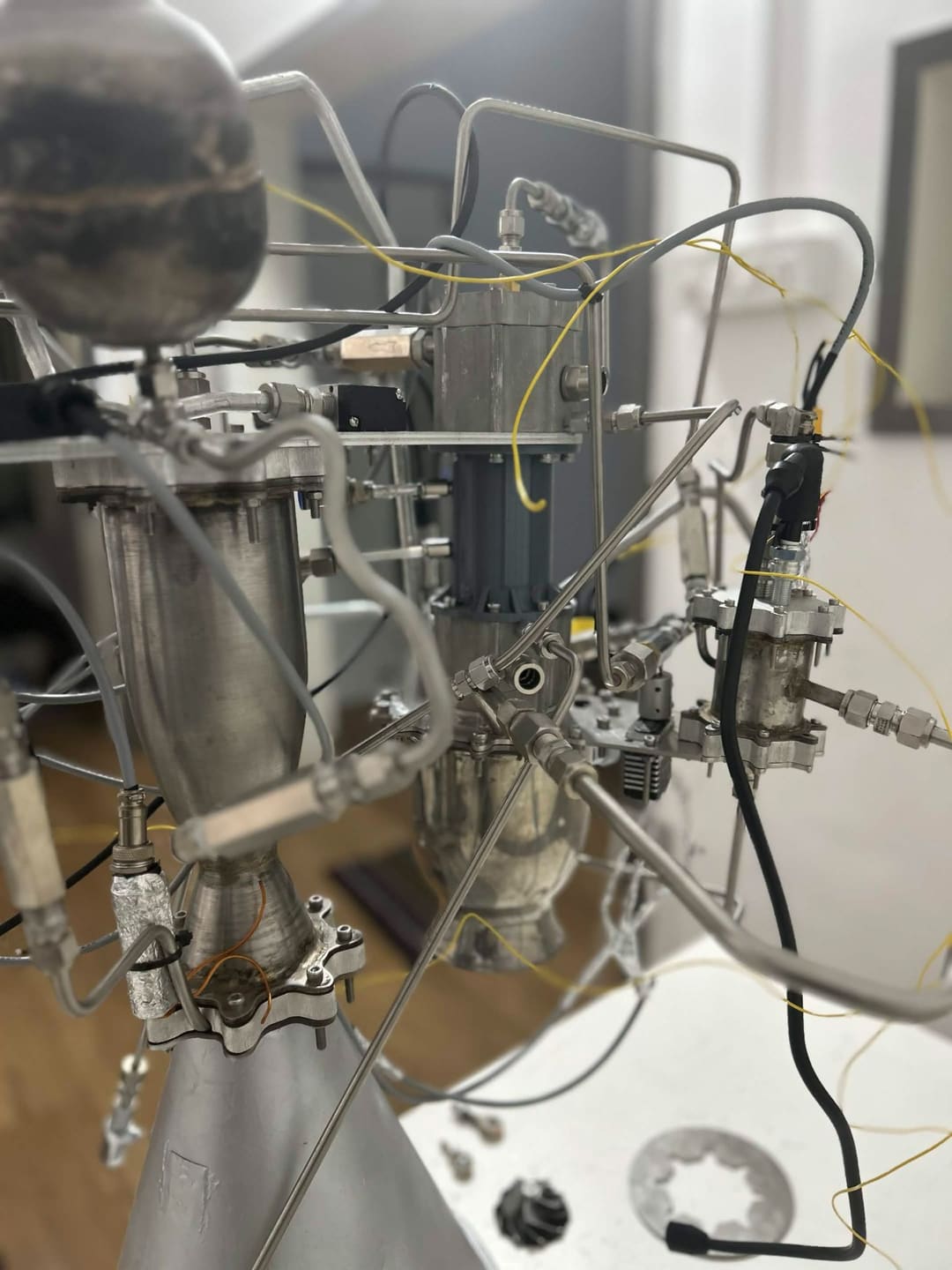 Detail of APEX propulsion development hardware: a spherical vessel in the foreground, metal assemblies, tubing and cabling behind.