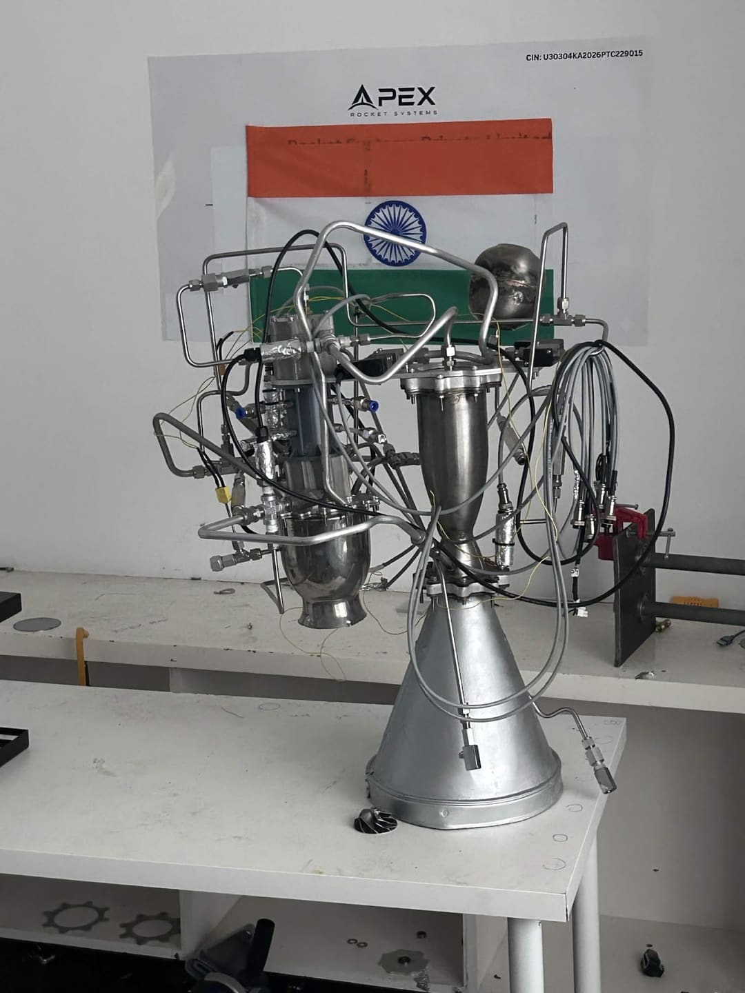 APEX propulsion development hardware on a white workbench, in front of an APEX Rocket Systems poster and the Indian flag.